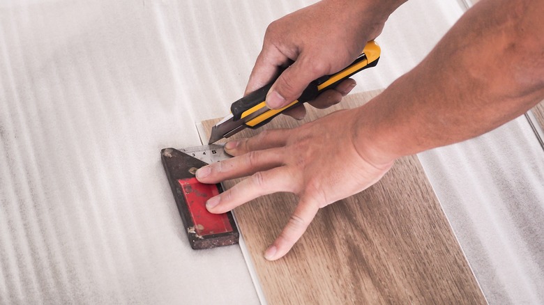 Hands cutting a vinyl plank with a utility knife